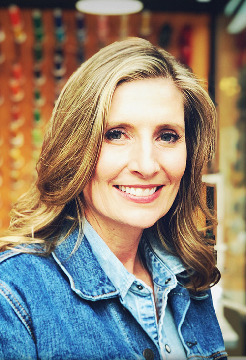 A woman with shoulder-length dirtly blonde hair wears a jean jacket and denim shirt.