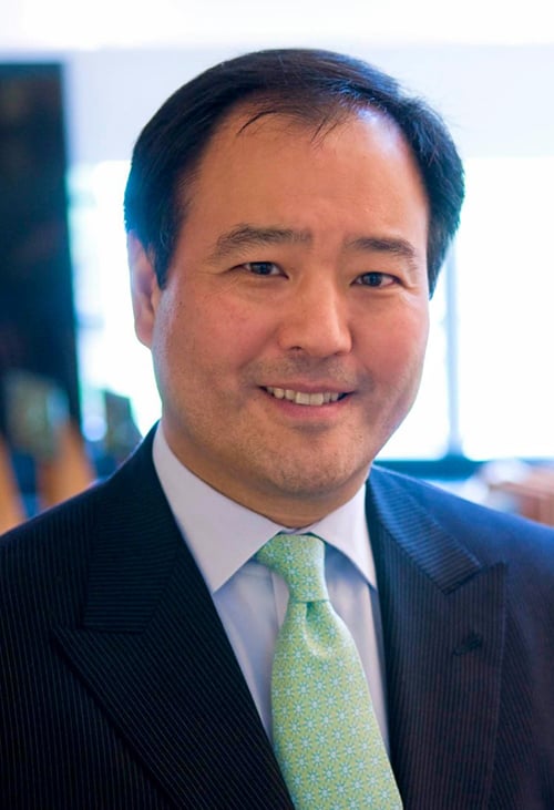 A man with dark hair smiles in a navy jacket with a pastel green tie.